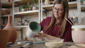 Woman pouring green paint into a container in a ceramics workshop. Preparing glaze for painting handmade clay pots, artisan working in a pottery studio - Powered by Shutterstock - Get 15% off with code: PIKWIZARD15