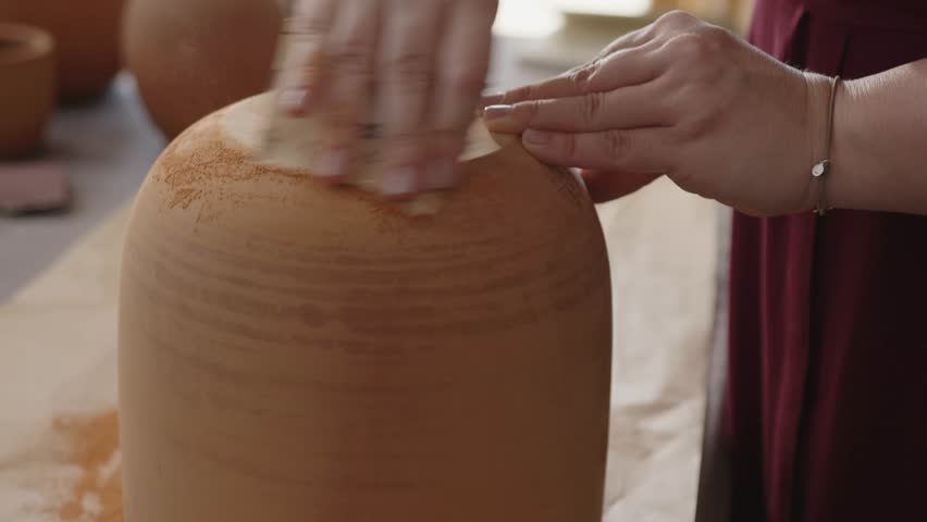 Woman sanding a clay pot in a ceramics workshop. Handmade pottery production process, artisan working with raw clay before painting.