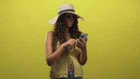 Woman holding smartphone pumps fist and smiles in studio wearing sunhat and sunglasses; joyful celebration. - Powered by Shutterstock - Get 15% off with code: PIKWIZARD15