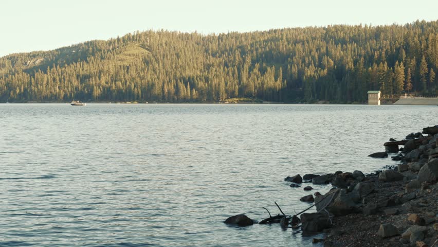 Lake shore with rocks and boat near forested hills