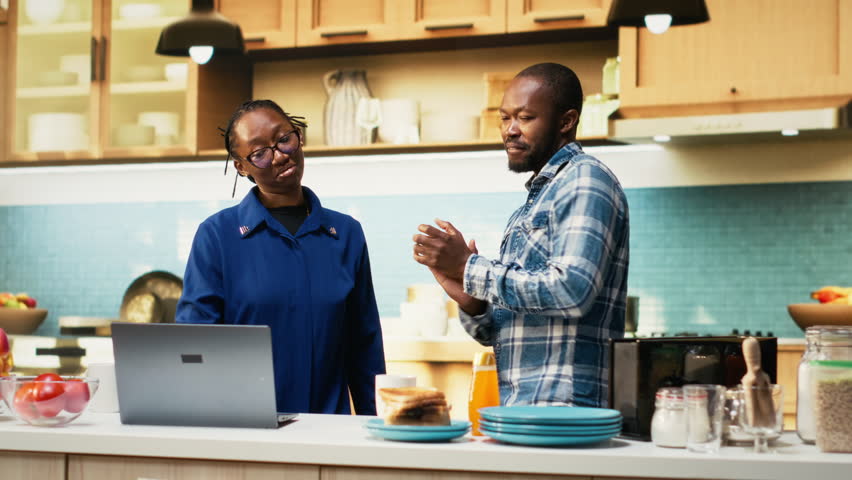 Boyfriend and girlfriend dancing indoors to upbeat music in the kitchen, making coffee and fooling around with silly enthusiastic energy. Playful couple show passion in comfortable home. Camera B.