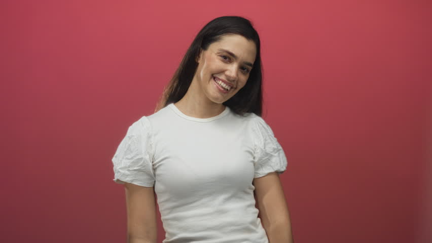 Hispanic woman in casual white shirt sticks tongue out with playful expression in red studio; silliness.