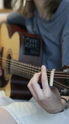Vertical clip of a teen casually playing acoustic guitar indoors, suitable for trending learning reels, beginner music education, and youth creative content