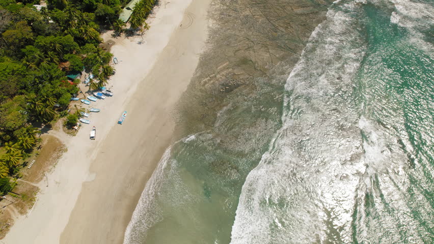 Aerial view of sandy beach with fishing boats and turquoise waves in Costa Rica