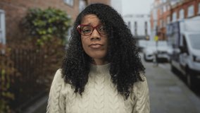 Woman squints eyes behind red glasses on a city street lined with brick buildings and parked white vans; skepticism. - Powered by Shutterstock - Get 15% off with code: PIKWIZARD15
