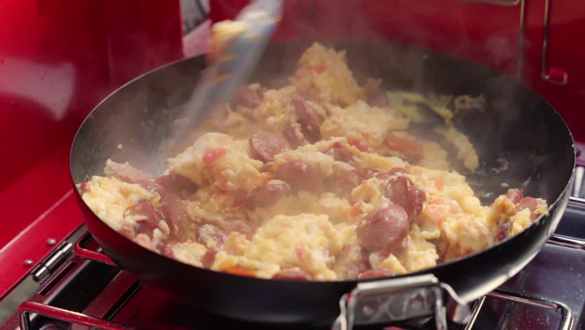 Horizontal video of a traveler cooking at a summer campsite, capturing relaxed outdoor adventure moments in warm natural light.