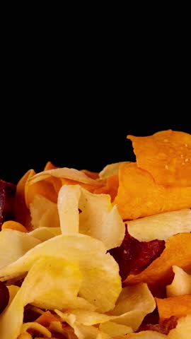 Hand picks assorted crispy root vegetable chips under bright lighting, close-up, black background, smooth motion