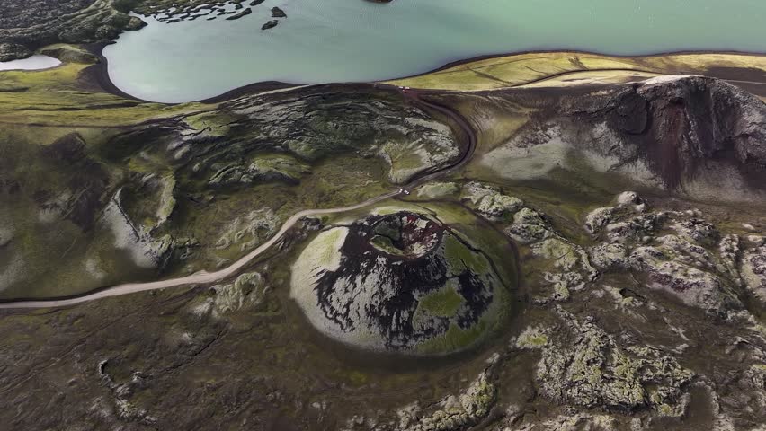 Stutur crater in Icelandic highlands during sunny day. Aerial tilt up wide shot. Blue glacial lake in background.