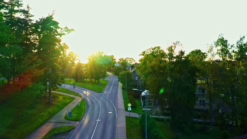 Serene road curving through forested town with sunset light and car passing