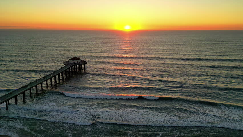 Aerial view of pier and waves during ocean sunrise near Manhattan Beach, California
