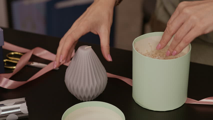 Tilt up shot of adult Caucasian woman in apron placing handmade candle in box while packing order in gift shop