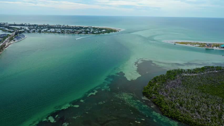 Tidal water from Lemon Bay flows toward the Gulf of Mexico through Stump Pass beside the mangrove shoreline near Manasota Key on Florida’s Gulf Coast, revealing sandbars and shifting textures.