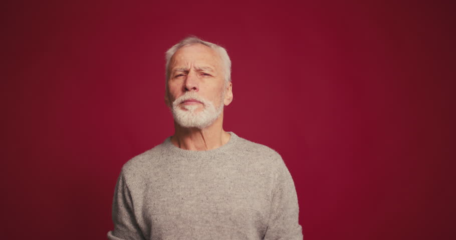 Portrait of serious pensive senior man showing thumbs up, nodding his head isolated on red background. Retired male posing in studio. Good choice concept