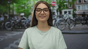 Girl with glasses smiles on a busy city street lined with bicycles wearing a light green shirt; youthful joy. - Powered by Shutterstock - Get 15% off with code: PIKWIZARD15