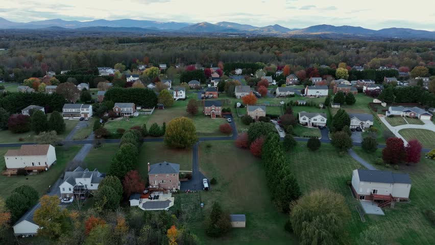 Ona family houses and homes in american suburb district at sunset time. Straight street with colorful trees on foliage autumn day. Aerial rise wide shot. Q