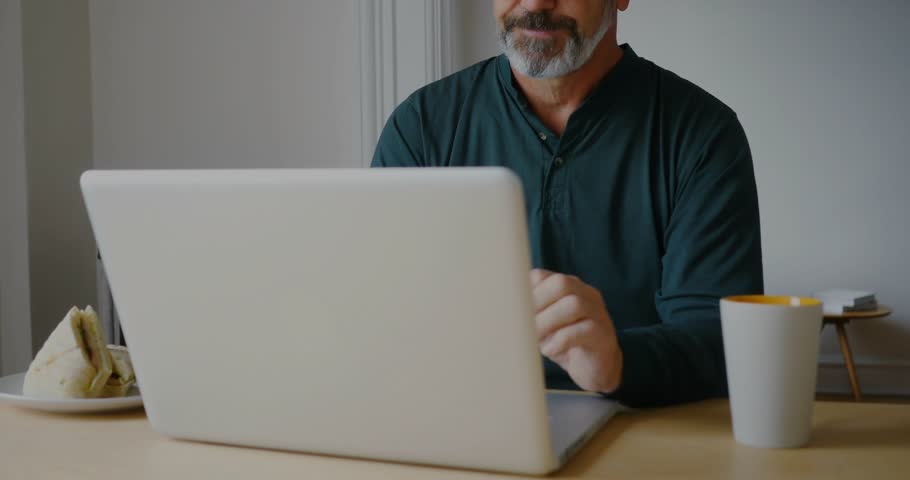 Man typing on laptop using trackpad at home office, invoking blue HUD analytics and code overlays. Remote, workspace, desk, focus, digital, waveforms, graphs