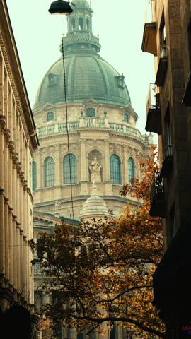 A view of St. Stephen’s Basilica framed between two buildings in Budapest, with autumn leaves and warm light creating a cinematic European city atmosphere.