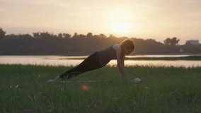 A woman practicing side plank yoga pose on grass during sunrise near a calm river landscape - Powered by Shutterstock - Get 15% off with code: PIKWIZARD15
