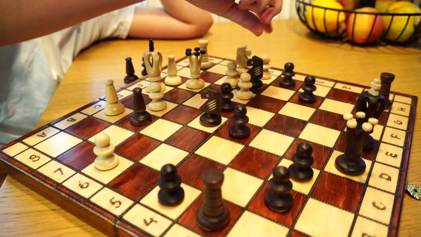 A closeup of a boy hand moving the queen piece on a chess board