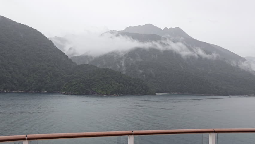 Milford Sound, Fiordland National Park, forested, steep mountains rising from dark fiord waters under low clouds and mist, creating moody, majestic, remote seascape