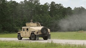 A military tactical vehicle is shown driving on a rocky track during an open-air training exercise. A soldier on top of the vehicle is seen firing a shot. - Powered by Shutterstock - Get 15% off with code: PIKWIZARD15