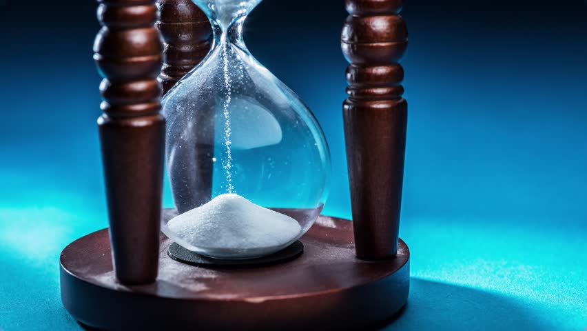 Wooden hourglass with white sand in the concept of fast current time. Blue background. Animation time lapse in 4K.