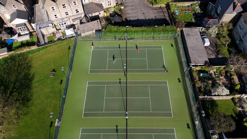 Clevedon Lawn Tennis Club with active match on artificial court surrounded by houses, gardens, and parking. 4K drone video from above.