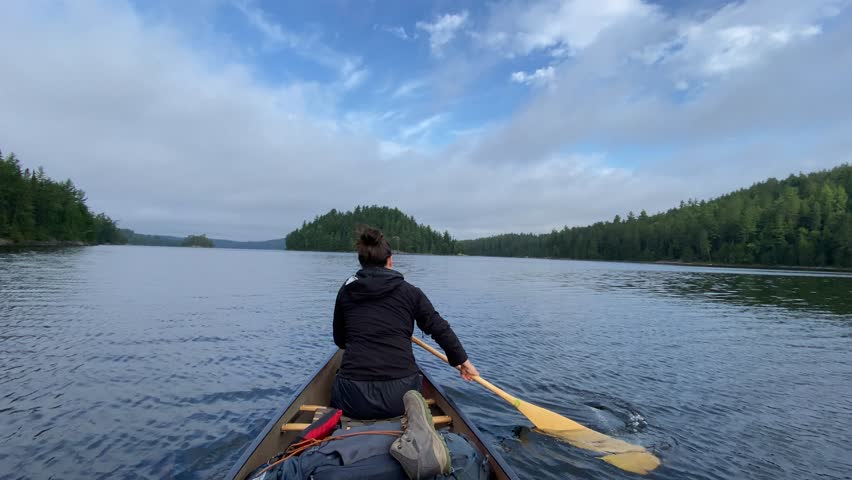 A back shot of a young woman on a canoe paddling on a serene lake in Ontario, Canada during daytime