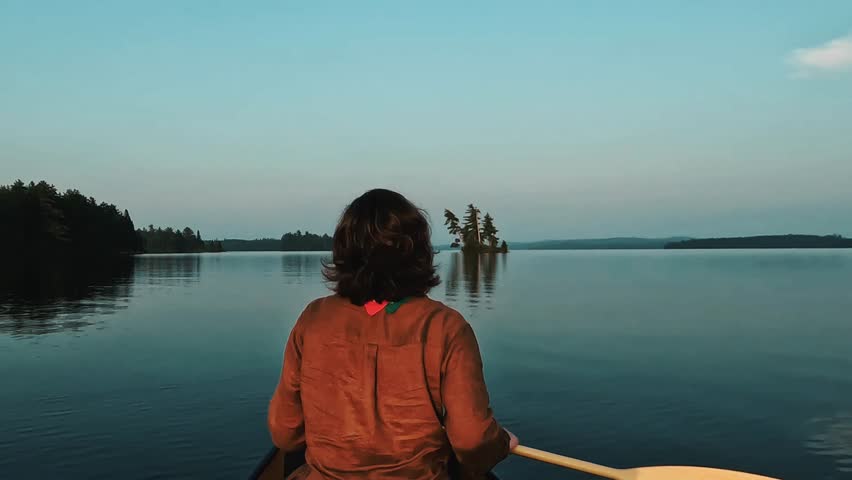 A woman paddles through a golden hourlight on a mirror-like lake in Algonquin Park. in stunning 4K