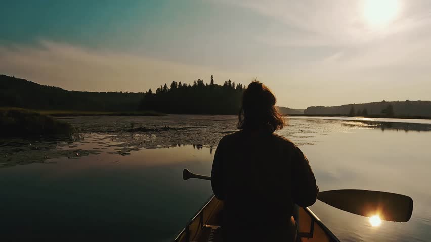A woman paddles through a golden hourlight on a mirror-like lake in Algonquin Park. in stunning 4K