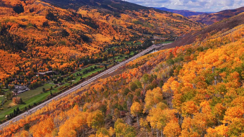 Vail Village Vail mountain ski resort ski trails morning aerial drone fall autumn vibrant colorful quaking aspen trees October blue sky clouds White River National Forest i70 highway cars forward pan