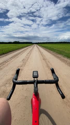 A vertical view of a bicycle while the cyclist riding on a dirt road with free hands in a rural landscape with a cloudy sky