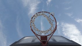 A slow-motion low angle view of a basketball hoop under blue sky with partial clouds, on a sunny day - Powered by Shutterstock - Get 15% off with code: PIKWIZARD15