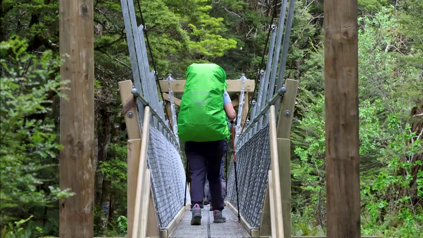 A back view of the hikers walking on a suspension pedestrian bridge in the Routeburn Track in Otago region in the South Island of New Zealand