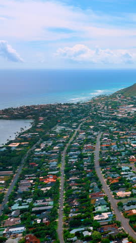 Housing in Honolulu near shoreline with lagoon on one side and volcanic hills on the other. Blue ocean gradient. Aerial view. Vertical video.