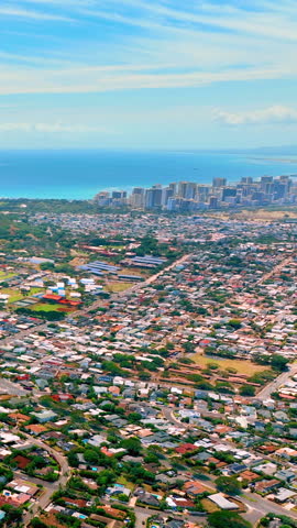 Low-rise buildings in the vicinity of Honolulu with downtown and skyscrapers on the horizon near the ocean coast. Aerial view. Vertical video.