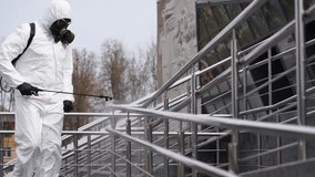 Worker in hazmat suit and gas mask sprays sanitizer on public railings, disinfecting touch surfaces to prevent Covid-19 spread during quarantine. - Powered by Shutterstock - Get 15% off with code: PIKWIZARD15