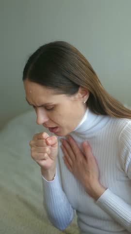 woman coughing, holding chest on bed, cold turtleneck, pained expression, respiratory symptom, woman coughing indoors, woman descent suffering from respiratory symptoms while resting on bed. vertical