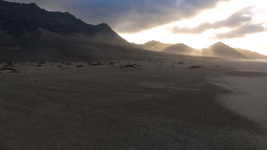 Aerial view of Cofete Beach, where sunbeams pierce through the clouds, casting an ethereal glow on the sand dunes and distant mountains, Cofete, Canary Islands, Spain.