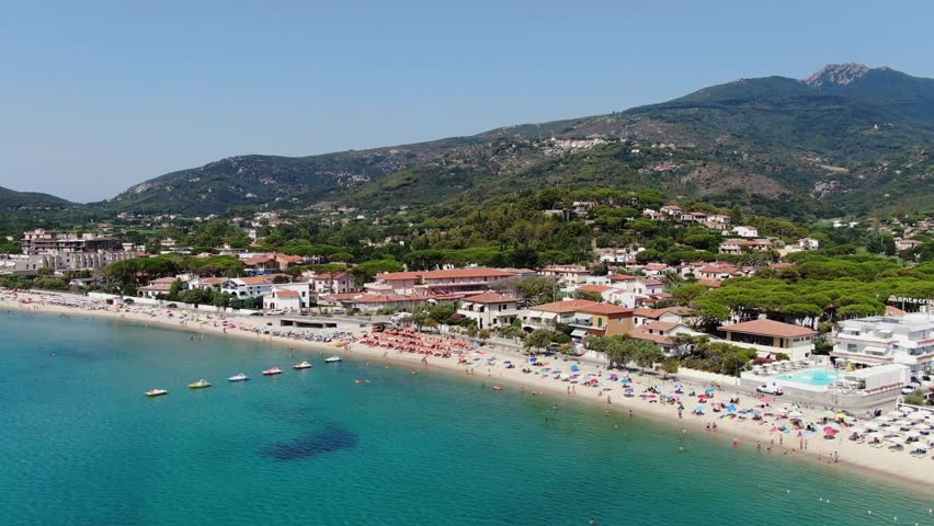 Boats bobbing in calm waters as people enjoy the sunny, vibrant shoreline of Isola d’Elba.