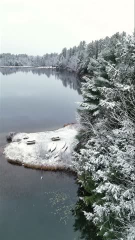 Aerial view of a snow-covered landscape with a serene lake surrounded by trees, a beach with canoes and picnic tables, White Mountains, New Hampshire, USA.
