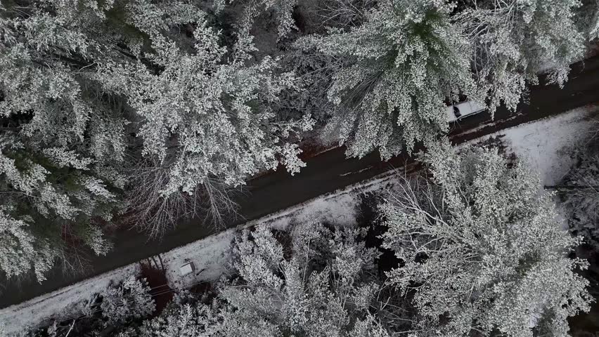 Aerial view of a dark road cutting through a forest of snow-covered trees, two cars visible on the road, White Mountains, New Hampshire, United States.