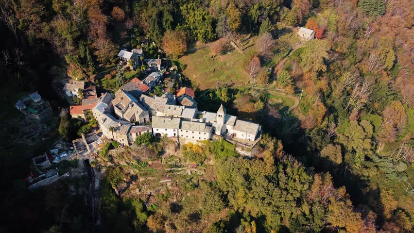 Aerial view of Carmine Superiore, a village with tightly packed stone buildings nestled into the mountainside surrounded by colorful autumn trees, Carmine Superiore, Piedmont, Italy.