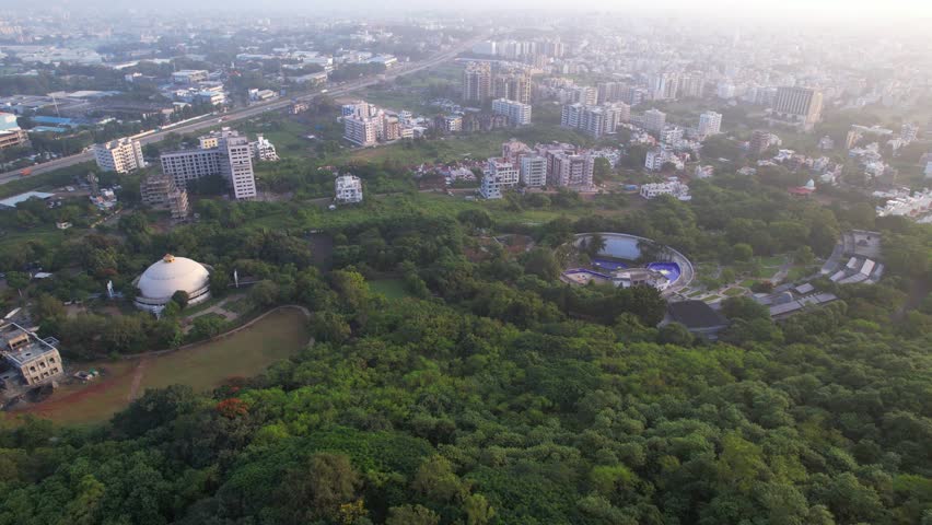 Tier 2 Nashik city residential and commercial highrise building surrounding greenery under hazy sky due to climate change and air pollution, establishing drone shot