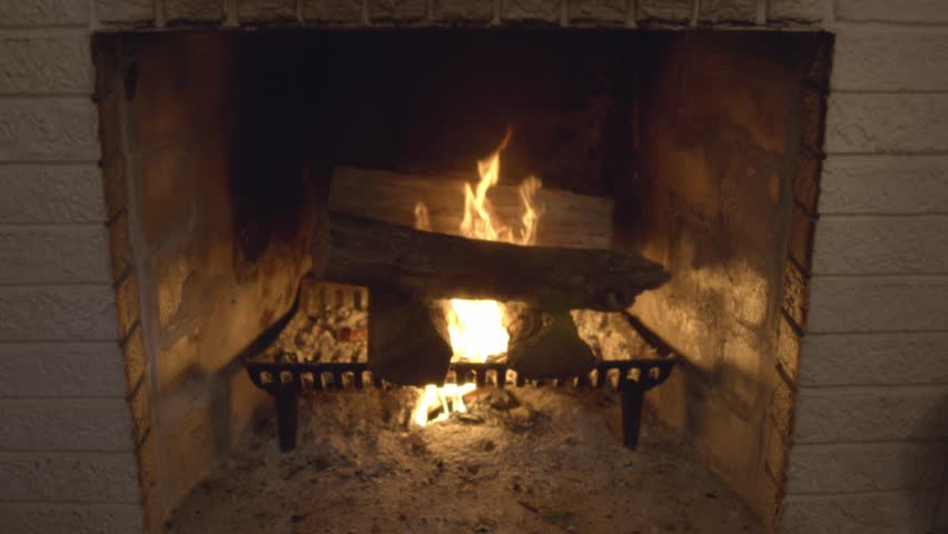 A roaring fire in a vintage brick fireplace in a cozy living room. Classic burning logs. Shot in 60 frames for slow motion.