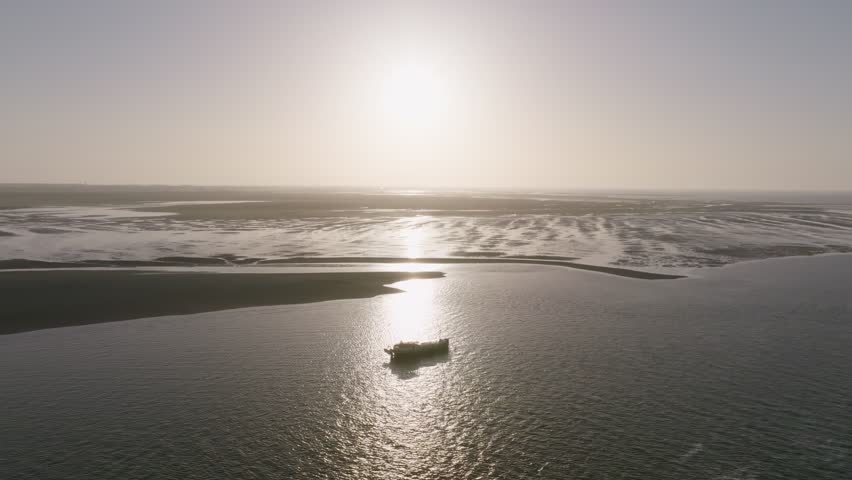 Pull in to wadden sea mudflats where a luxemotor boat sits near sandbanks with strong sun glitter.