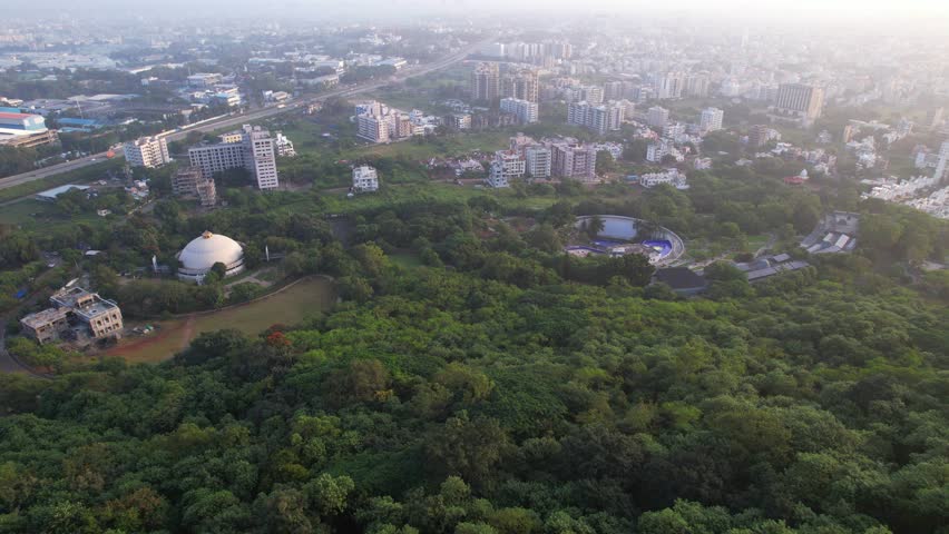 Tier 2 Nashik city greenery with residential and commercial highrise buildings under hazy sky due to climate change and air pollution, drone shot