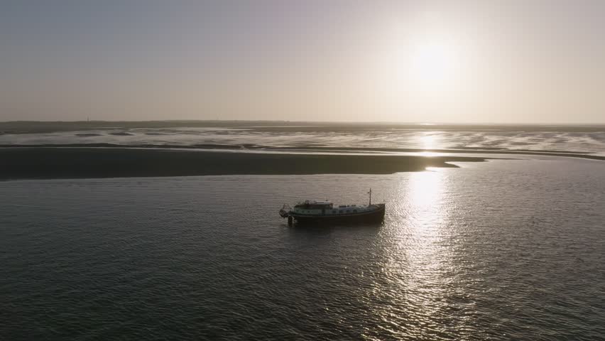 Oblique shot of a luxemotor boat floating in shallow water adjacent to the wadden sea under strong morning sun.