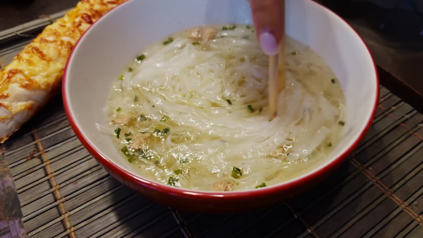 Eating Rice Noodles In Clear Broth With Chopsticks, Delicious Asian Soup Meal, Hand Holding Chopsticks Over Bowl. Authentic Southeast Asian Flavors. Vietnamese Pho Or Ramen. Traditional Asian Cuisine
