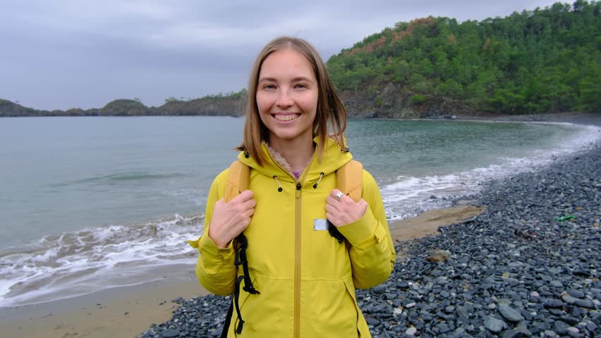Young woman walks alone along cold Turkish coast. Windy, cloudy weather, peaceful solitude and gentle connection with nature by stormy sea.